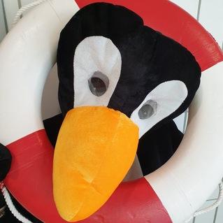 Ein Pinguin-Kost&uuml;m h&auml;lt einen roten und wei&szlig;en Rettungsring in einer Umgebung mit gefliesten W&auml;nden.