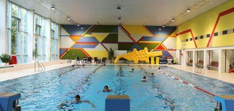Schwimmbecken in einem Hallenbad mit bunten W&auml;nden und mehreren Personen im Wasser. Rutschbahn an der Seite.