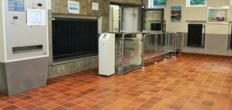 Men&uuml; mit Ticketautomat und Drehkreuz in einem hellen Innenraum mit Fliesenboden und Fenster.