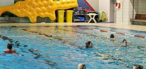 Schwimmerinnen genie&szlig;en das Wasserspiel in einem Hallenbad mit einer gelben Riesenrutsche im Hintergrund.