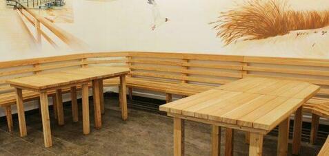 Holzbank und Tische aus unbehandeltem Holz in einem Raum mit einfarbiger Wandgestaltung und minimalistischem Ambiente.