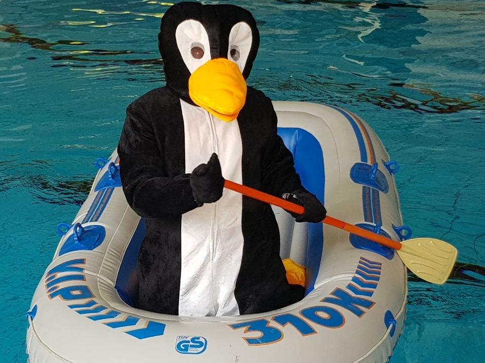 Pinguin-Kost&uuml;mtr&auml;ger paddelt in einem aufblasbaren Boot in einem Schwimmbecken.